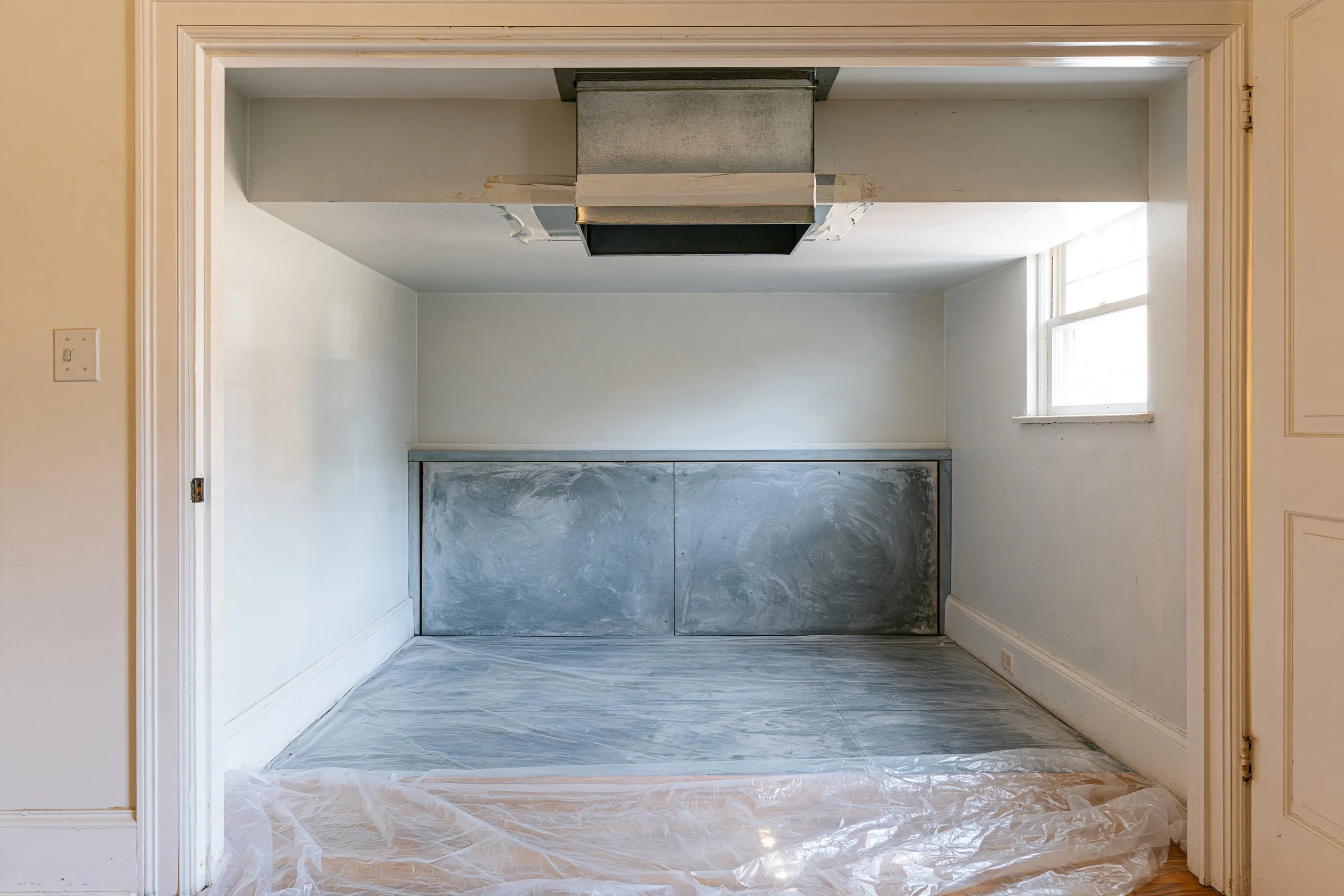 Hall closet with the old furnace gone, a duct collar sealed with old white tape and a gray cement-board panel