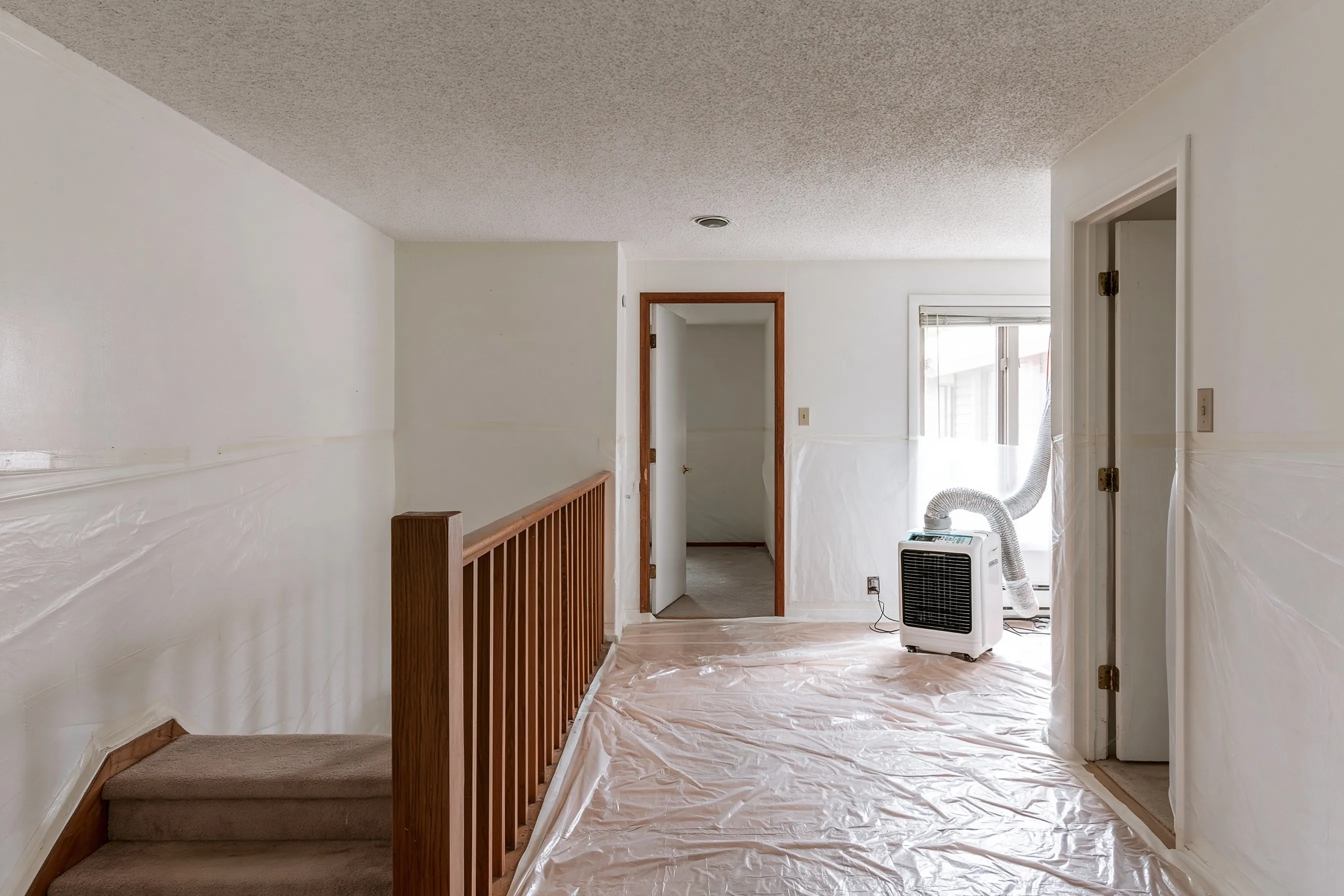 Upstairs of a 1960s split-level with a painted popcorn ceiling, plastic on the floor and walls and the short stair in view